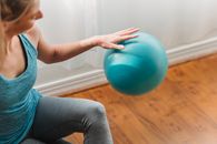Cheerful fit female gymnast training with ball on parquet