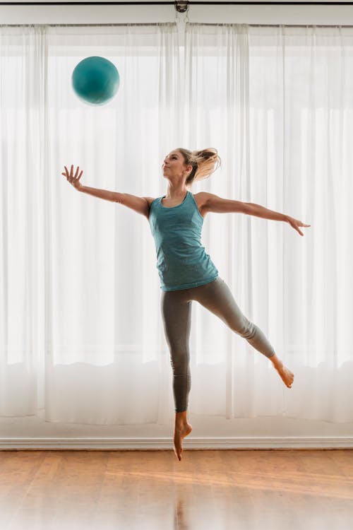 Free Fit female in sportswear jumping up and throwing fit ball during workout in modern studio Stock Photo