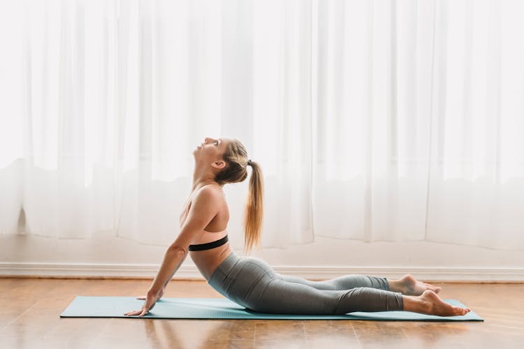 Flexible Young Woman Doing Bhujangasana Yoga Pose In Studio