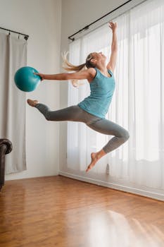 Dynamic shot of a fit woman jumping indoors with a fitness ball, showcasing energy and athleticism.