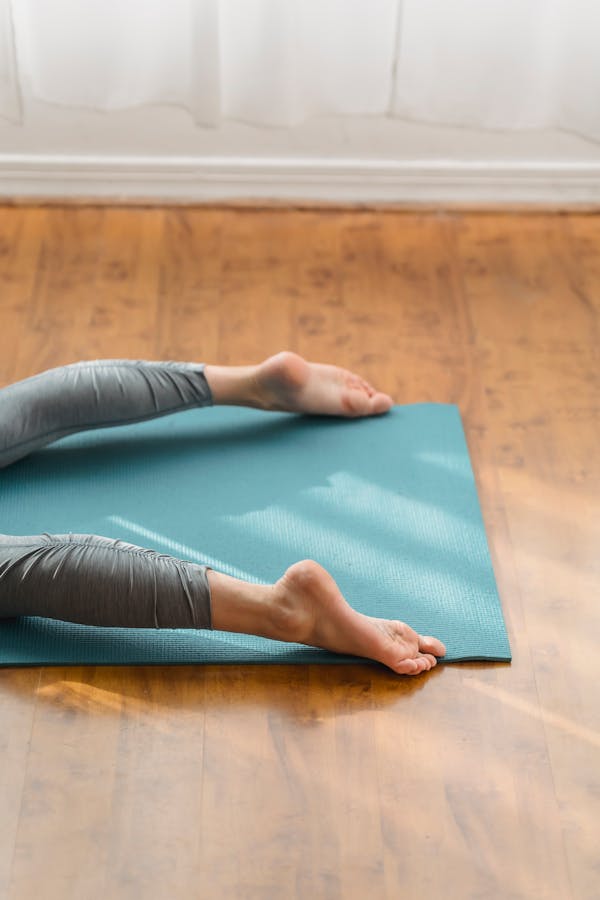 From above of crop unrecognizable barefooted female in leggings lying prone on mat while practicing yoga in studio