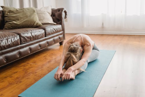 Anonymous female yogi doing Pascimottanasana stretching exercise on mat at home