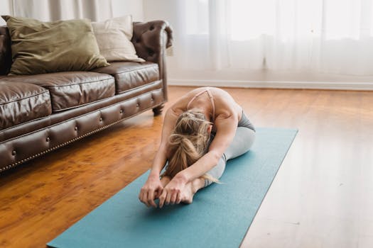 Woman doing yoga in a living room, focusing on a seated forward bend pose for wellness.