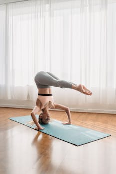 Full length of determined young female in sportswear performing Supported Headstand with Legs Halfway Down on mat during Ashtanga Vinyasa yoga training in light room