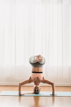 A flexible young woman practicing yoga headstand indoors on a yoga mat.