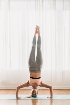 Woman performing a headstand yoga pose indoors on a mat, showing flexibility and balance.