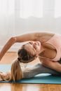 Graceful young female with long blond hair in activewear sitting on mat and stretching body in Revolved Head to Knee yoga pose in light studio
