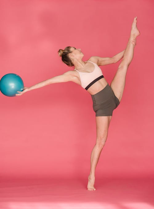 Woman on tiptoe doing split and exercising with fitness ball