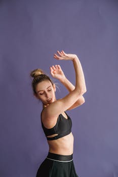 Graceful young woman dancer posing in sportswear against a purple background.