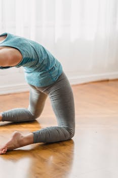 Woman in activewear stretching with a backbend pose indoors on a wooden floor.