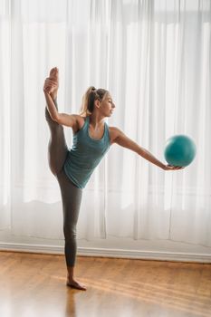 Full body of flexible female athlete doing standing split with fitness ball on outstretched arm