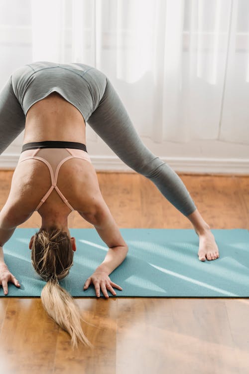 Unrecognizable sportive female in activewear practicing headstand preparation posture while standing on mat during yoga training in light room at home