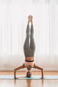 A woman performs a headstand on a yoga mat inside, showcasing balance and strength.