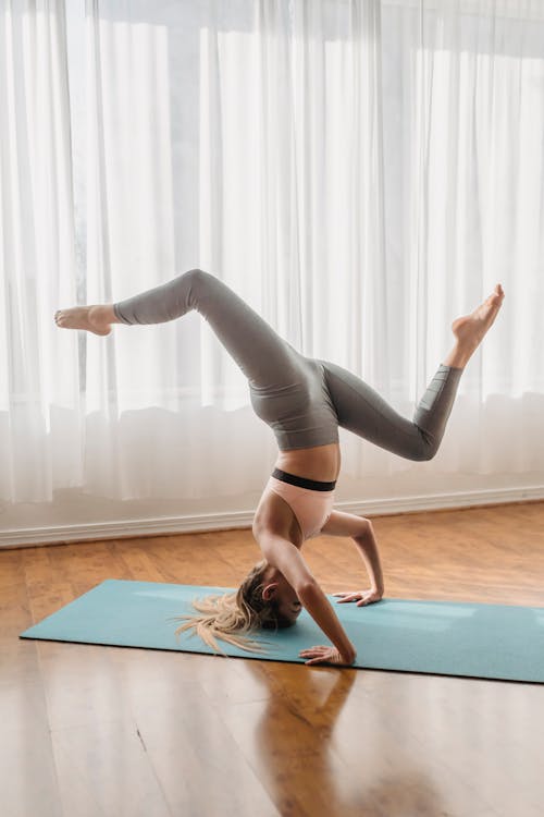 Full body side view of sportive unrecognizable female practicing Tripod headstand with spiral legs on mat during yoga training in room