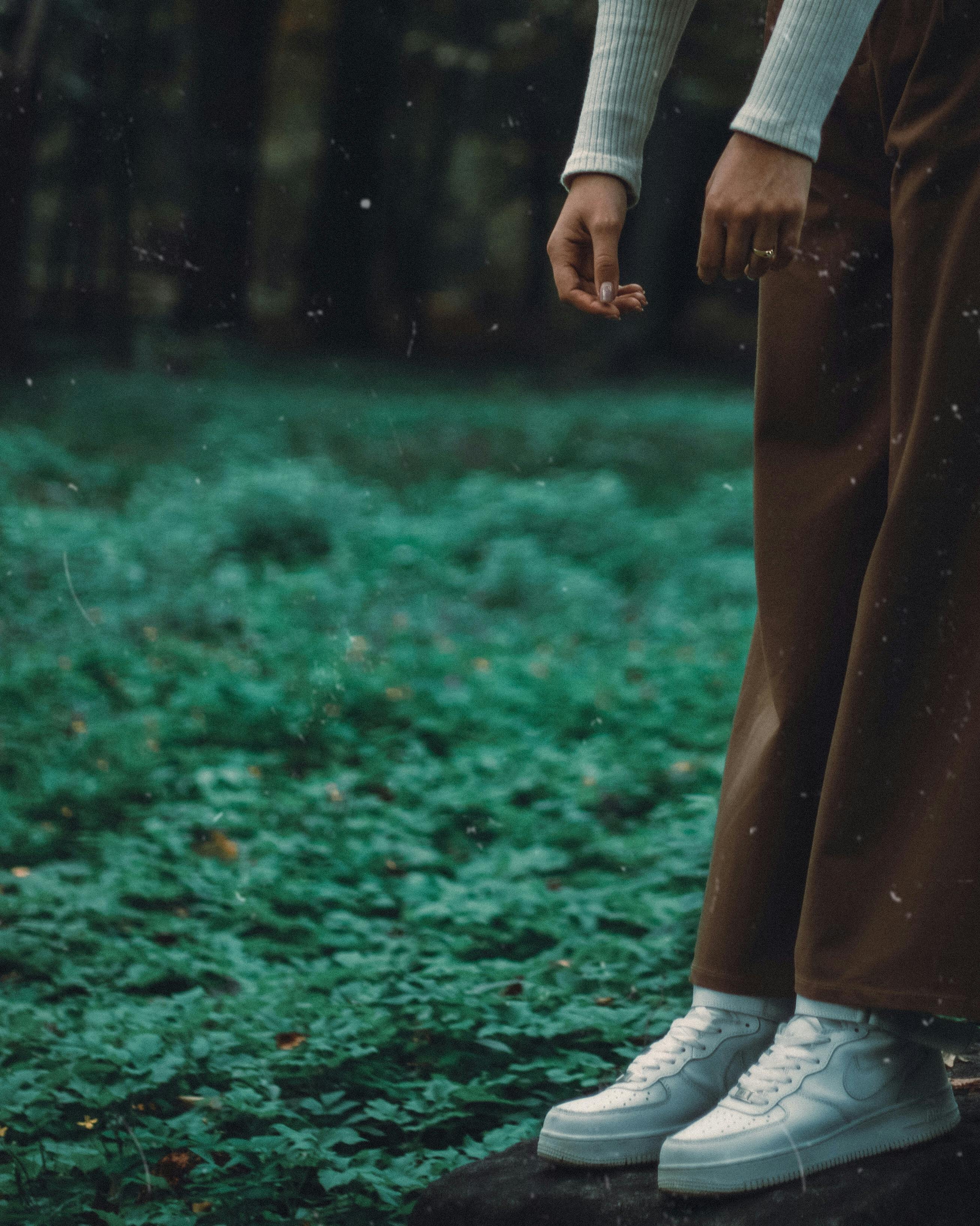 Person standing with white sneakers on a lush forest floor, showcasing urban style.