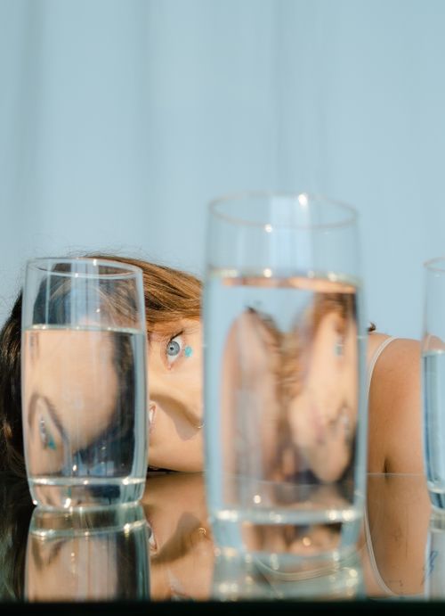 Free A brunette woman with blue eyes seen through and reflected in glasses of water. Stock Photo