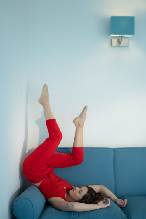 Free A woman in red lounging on a blue couch with feet up against a wall. Stock Photo