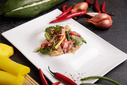 Free A vibrant Asian salad featuring noodles, fresh herbs, and chilies on a white plate. Stock Photo