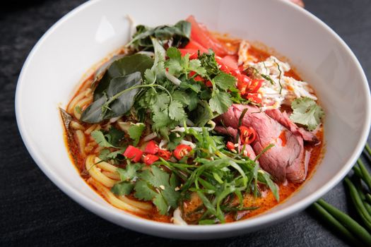 A vibrant and spicy Asian noodle soup featuring fresh herbs, beef, and chili peppers in a white bowl.