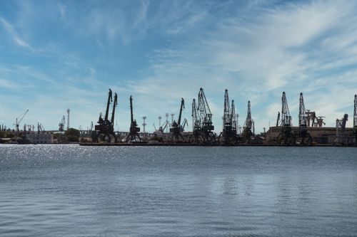 Free Panoramic view of a seaside construction site featuring industrial cranes and blue sky. Stock Photo