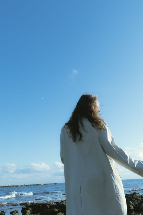 Free A woman stands by the ocean under a clear blue sky, enjoying a calm seascape. Stock Photo