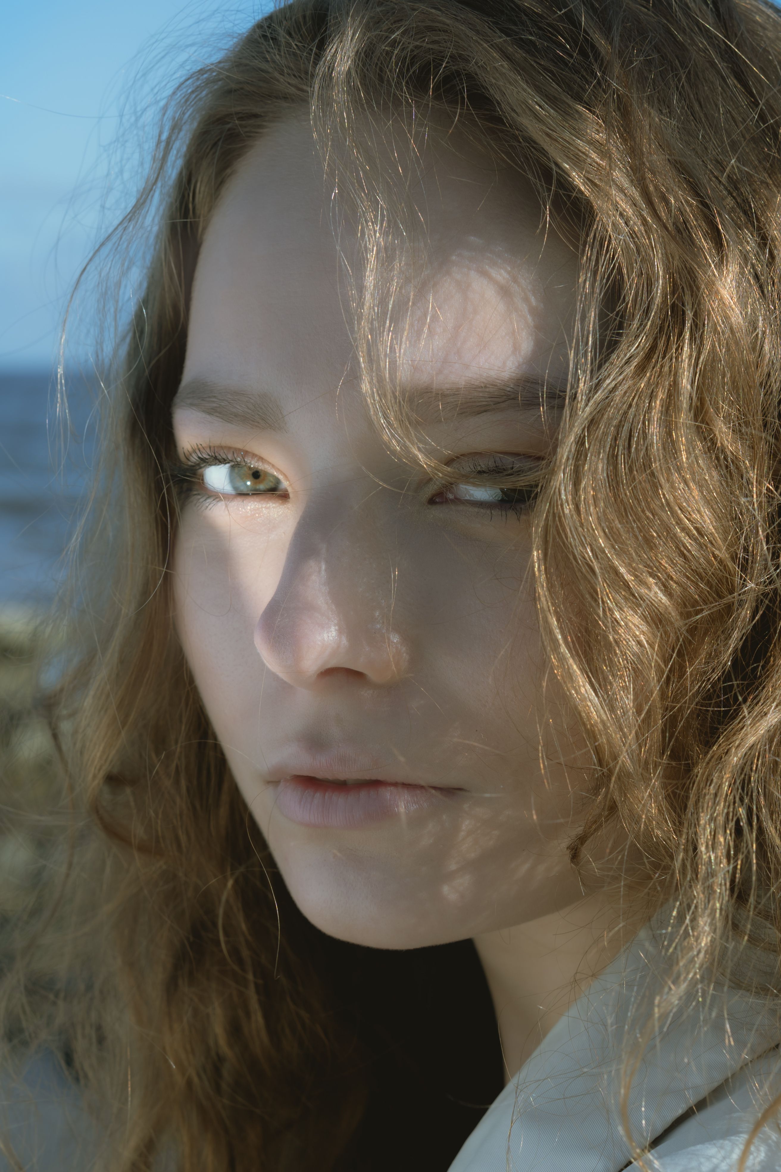 Close-up portrait of a woman with wavy hair and natural makeup, gazing softly at the camera outdoors.