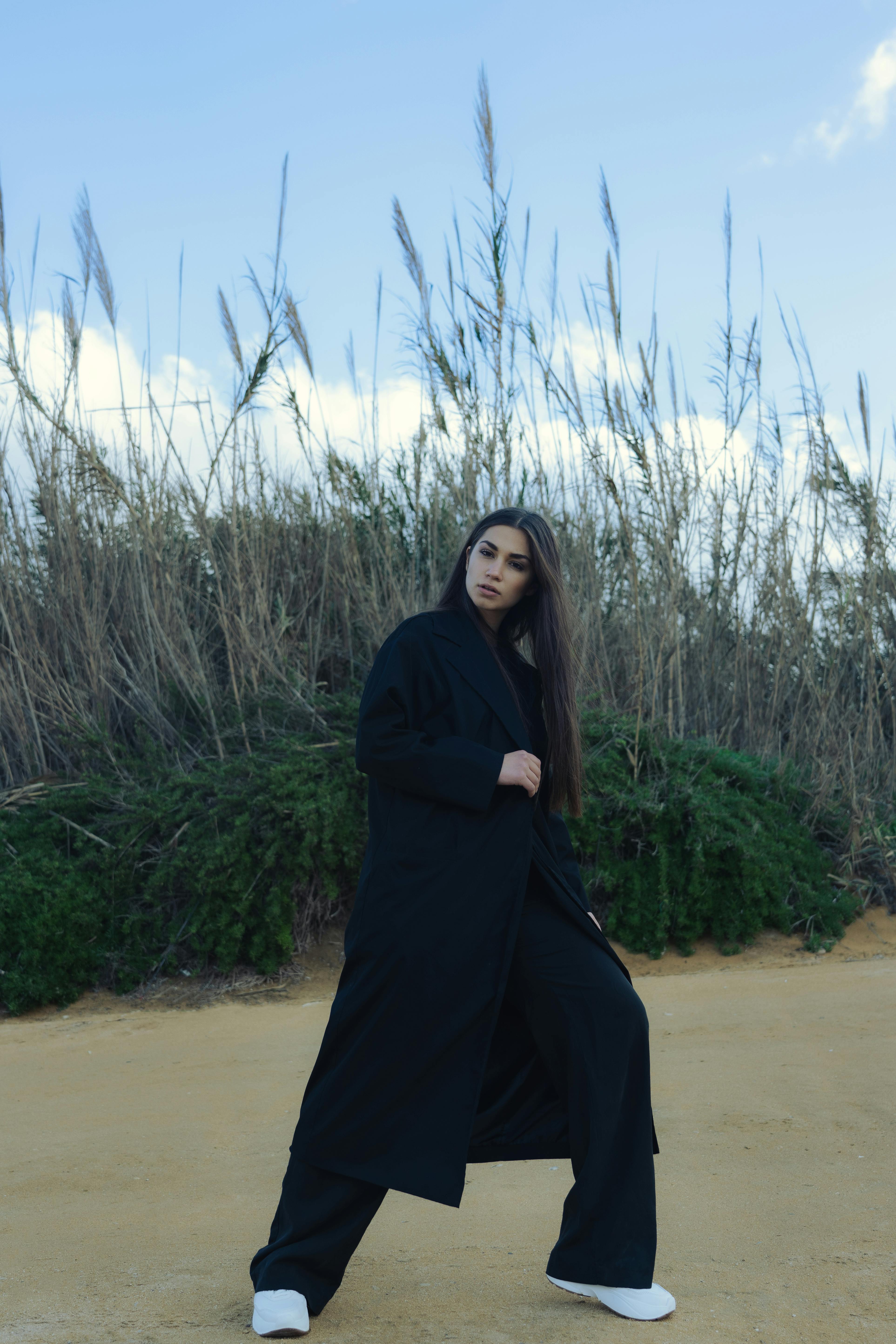 woman in black coat and pants standing on brown sand