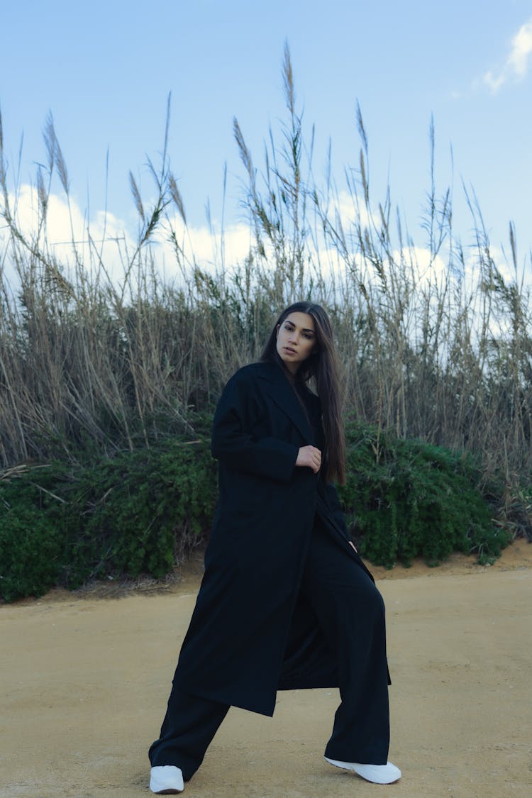 Woman In Black Coat And Pants Standing On Brown Sand