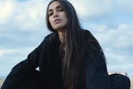 一位留着长发的沉思女子穿着黑色衣服在户外摆姿势，散发着宁静而内省的情绪