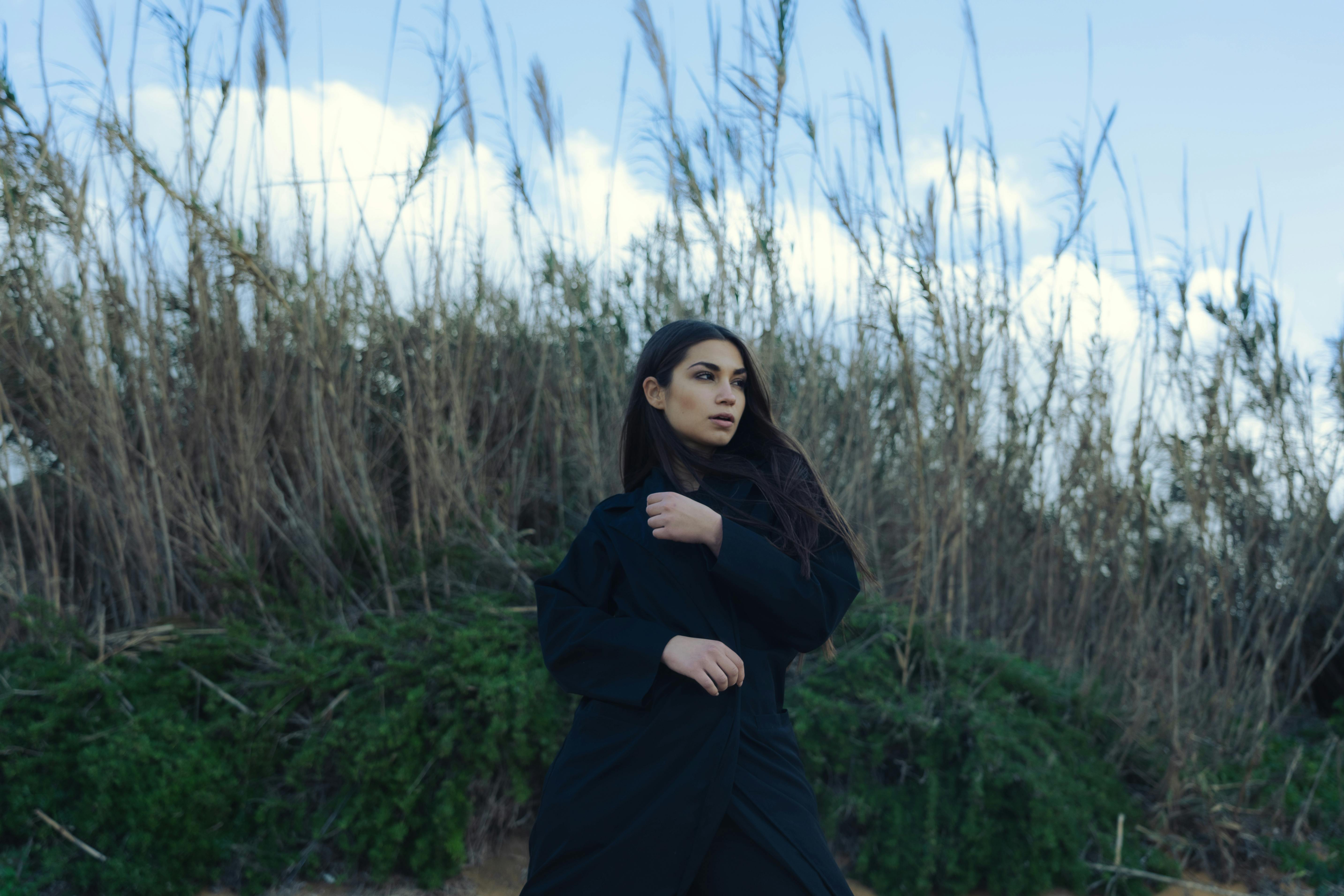 一名身穿黑色外套的女子在高高的草丛和蓝天的背景下在户外摆姿势