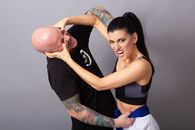 Angry sportswoman fighting with tattooed man on gray background