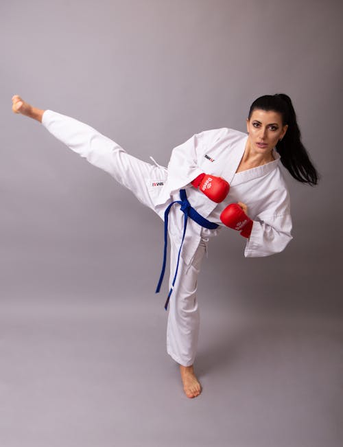 Young confident sportswoman in white sports clothes and gloves showing striking technique while looking at camera on gray background