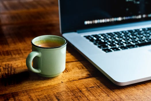 Close-up of a coffee mug next to a laptop on a wooden table, creating a cozy atmosphere.