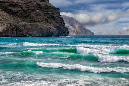 Ocean Waves Crashing on Brown Rock Formation Under White Clouds