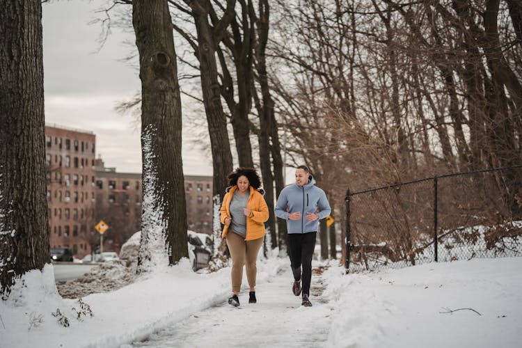 Diverse Male Trainer And Woman Jogging In Winter Park