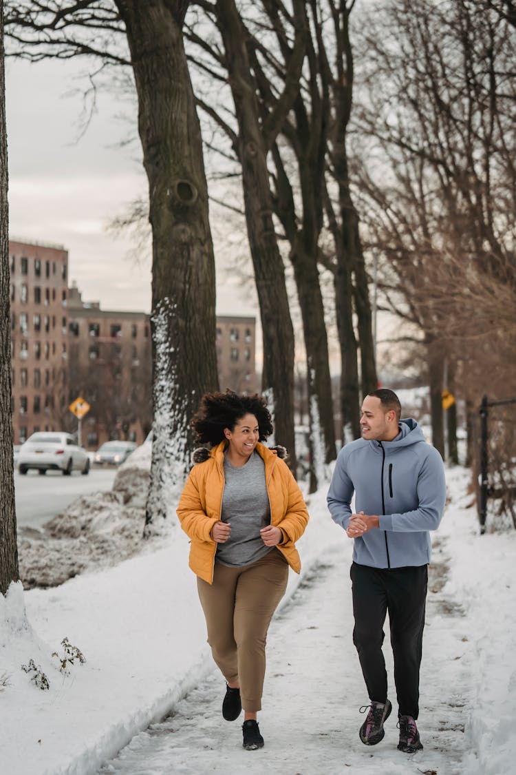 Cheerful Trainer And Black Woman Running In Winter City Park