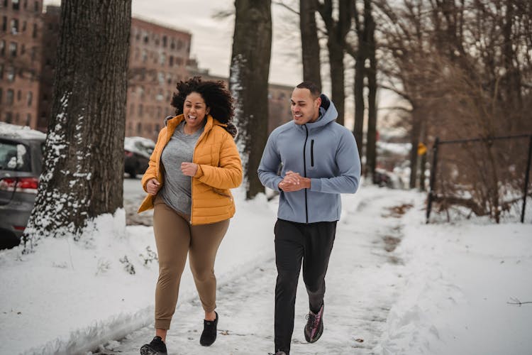 Happy Diverse Trainer And Woman Jogging In Winter Park