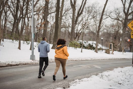 Back view anonymous fit male trainer and plus sized female with curly hair wearing warm clothes jogging together on roadway in snowy winter suburb