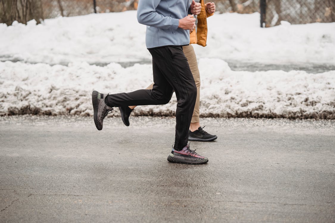 Free Crop unrecognizable sportspeople jogging on snowy roadway Stock Photo