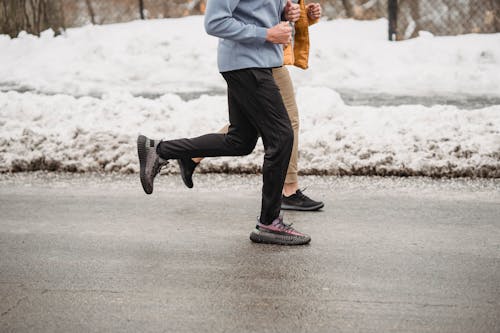 Crop unrecognizable sportspeople jogging on snowy roadway