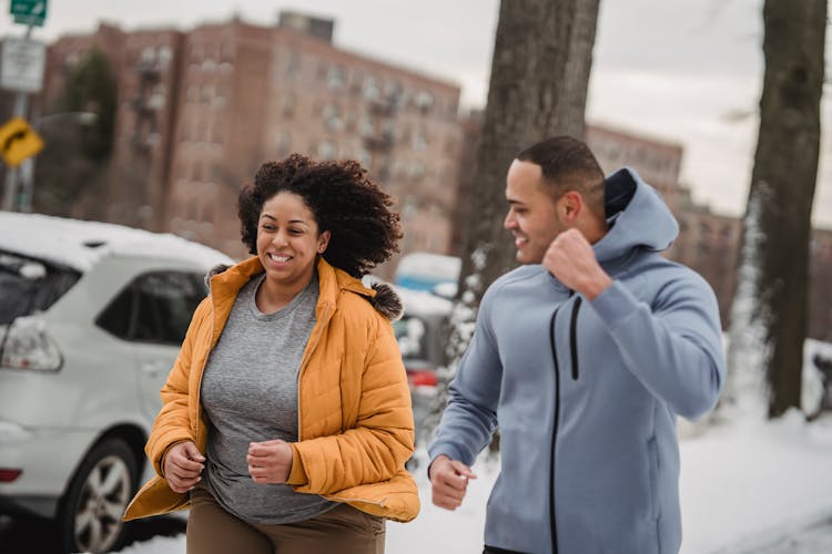 Cheerful Multiethnic Man And Woman Jogging On Winter City Street