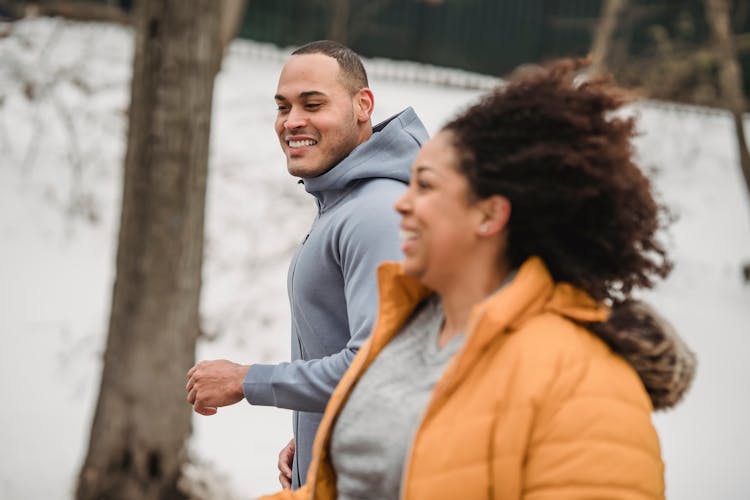 Happy Ethnic Man And Woman Jogging On Snowy Street