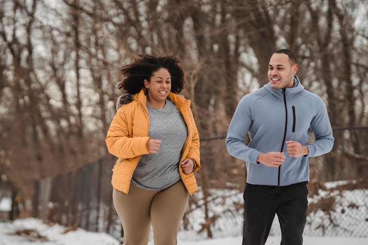 Cheerful Multiethnic Man And Woman Running Together In Winter Park