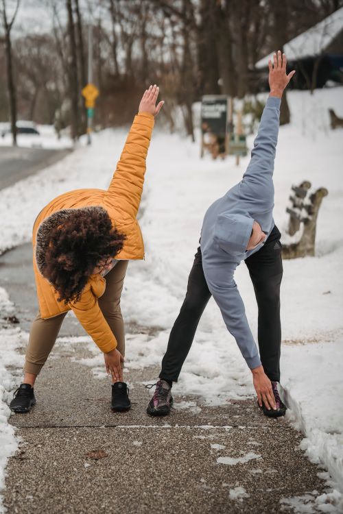 Free Full body faceless male trainer and overweight female performing windmill arm exercise while working out on snowy sidewalk on winter day Stock Photo