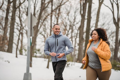 Diverse fit man and plump female running in snowy park