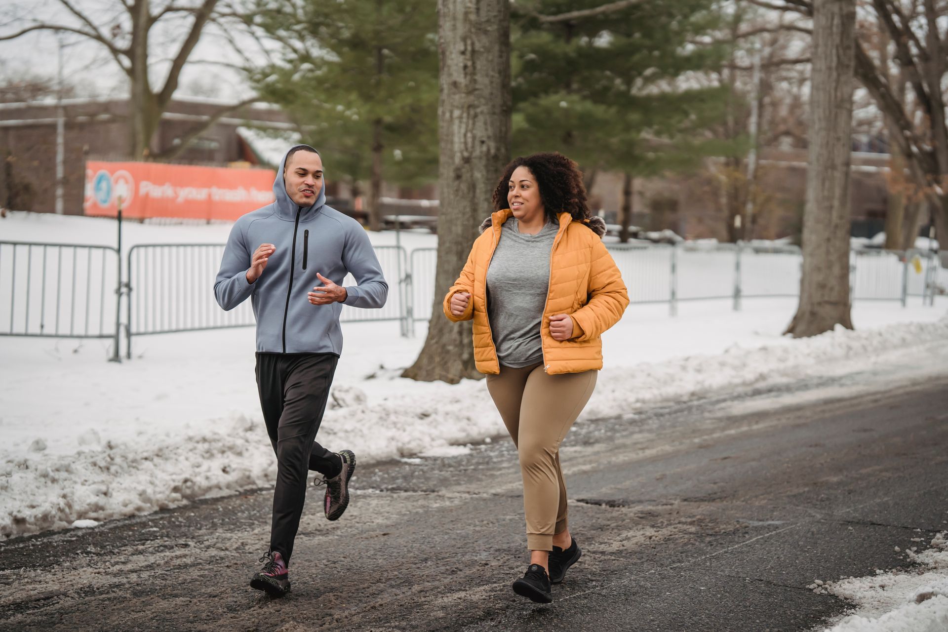 Two adults jogging in a snowy park during winter to maintain fitness and wellbeing.