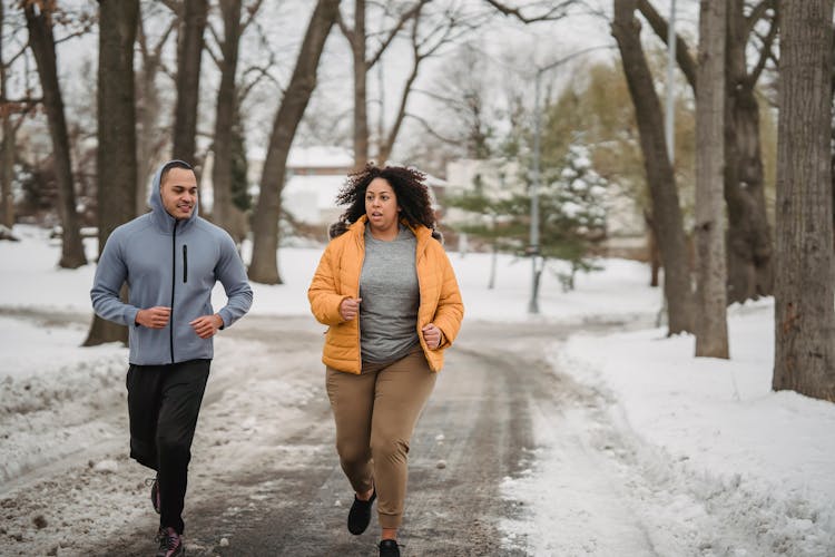 Overweight Black Woman Running With Trainer On Snowy Road