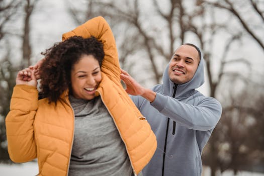 Black cheerful personal instructor helping overweight African American female to do stretching exercise in winter park on blurred background during training