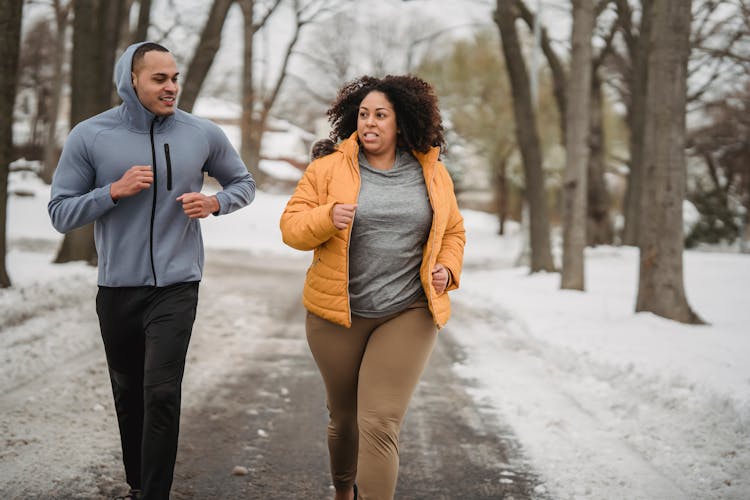 Determined Plump Black Woman Jogging With Trainer On Pathway