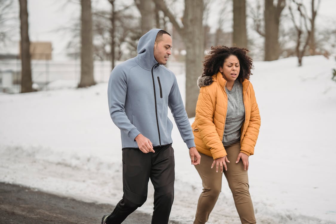 Exhausted plump African American female in outerwear with black personal instructor on pathway in snowy park during training in winter time